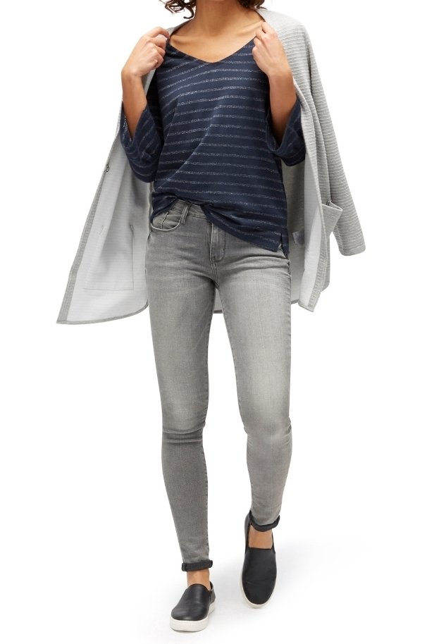 Top a righe navy a maniche lunghe, cardigan grigio, jeans skinny grigio chiaro e scarpe slip-on nere. Outfit casual con texture sovrapposte.