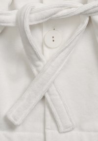 Vit klädnad gjord av mjukt tyg, med en omslagsdesign, ett tygband och en rund knappstängning. Texturen verkar fluffig och mysig.