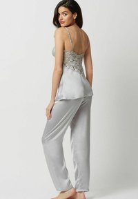 Pyjama en satin gris avec un dos en dentelle, des bretelles fines et un pantalon ample avec une texture lisse. Aucun motif notable.