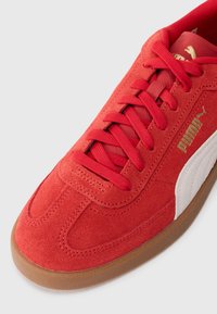Røde ruskinds sneakers med flade snørebånd, hvid accentstribe og gummibund. Har prægede logoer og struktureret overdel.