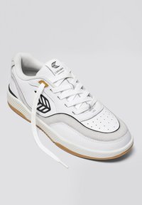 Sneaker in pelle bianca con accenti grigi, caratterizzata da un logo nero, punta perforata e suola in gomma. I lacci sono parzialmente slacciati.