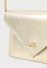Bolsa de mão em estilo envelope metálico dourado, com uma alça de corrente e um detalhe decorativo em tom dourado na frente, com uma textura suave.