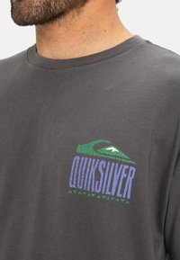 Grijze katoenen T-shirt met een kleurrijk Quiksilver-logo met groene en blauwe accenten, textuurdetails en een klassieke ronde hals.