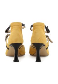 Gelbe Wildleder-Pumps mit einem schwarzen Riemen und einer Schnalle, mit einer abgerundeten Zehenpartie und einem geschwungenen schwarzen Absatz.