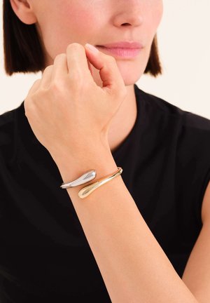 Silver and gold double bracelet featuring smooth, curved shapes with a polished metallic finish, showing sleek design and modern accents.