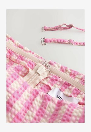 Rózsaszín és krém színű kockás anyag, textúrált felülettel. Cipzárral és fém hardware-ral ellátott állítható pántokkal rendelkezik. Címke látható.