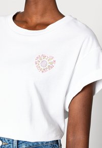 White cotton t-shirt featuring a colorful sun-inspired graphic with text "Live By The Sun" in pink and yellow, relaxed fit, short sleeves.