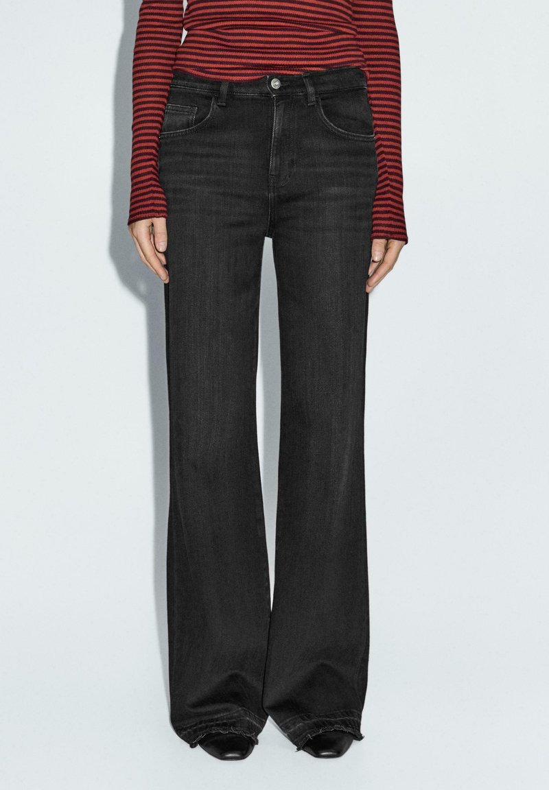 Jeans neri a gamba larga, materiale in denim, vita media, design a cinque tasche, orlo sfrangiato, abbinati a una maglia a maniche lunghe a righe rosse e nere.