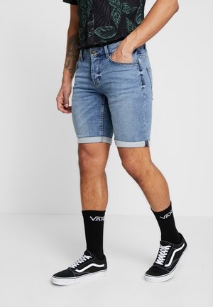 Shorts de mezclilla con un lavado azul claro, dobladillo en los extremos y un corte estándar. Combinados con zapatillas negras y calcetines de longitud media con logotipo.
