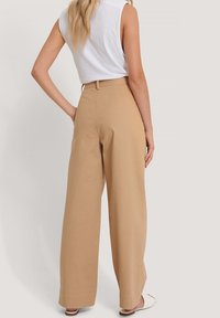 Beżowe spodnie o szerokich nogawkach z wysokim stanem, wykonane z lekkiego materiału. Posiadają subtelną teksturę i boczne kieszenie. Wyświetlany widok z tyłu.