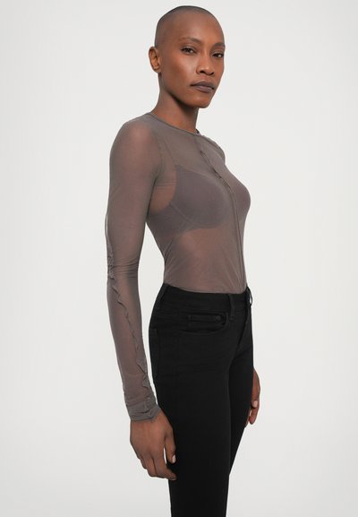 Langärmliges, durchsichtiges braunes Oberteil mit rundem Ausschnitt und Knopfverschluss. Kombiniert mit engen schwarzen Jeans. Weiche Textur und enge Passform.