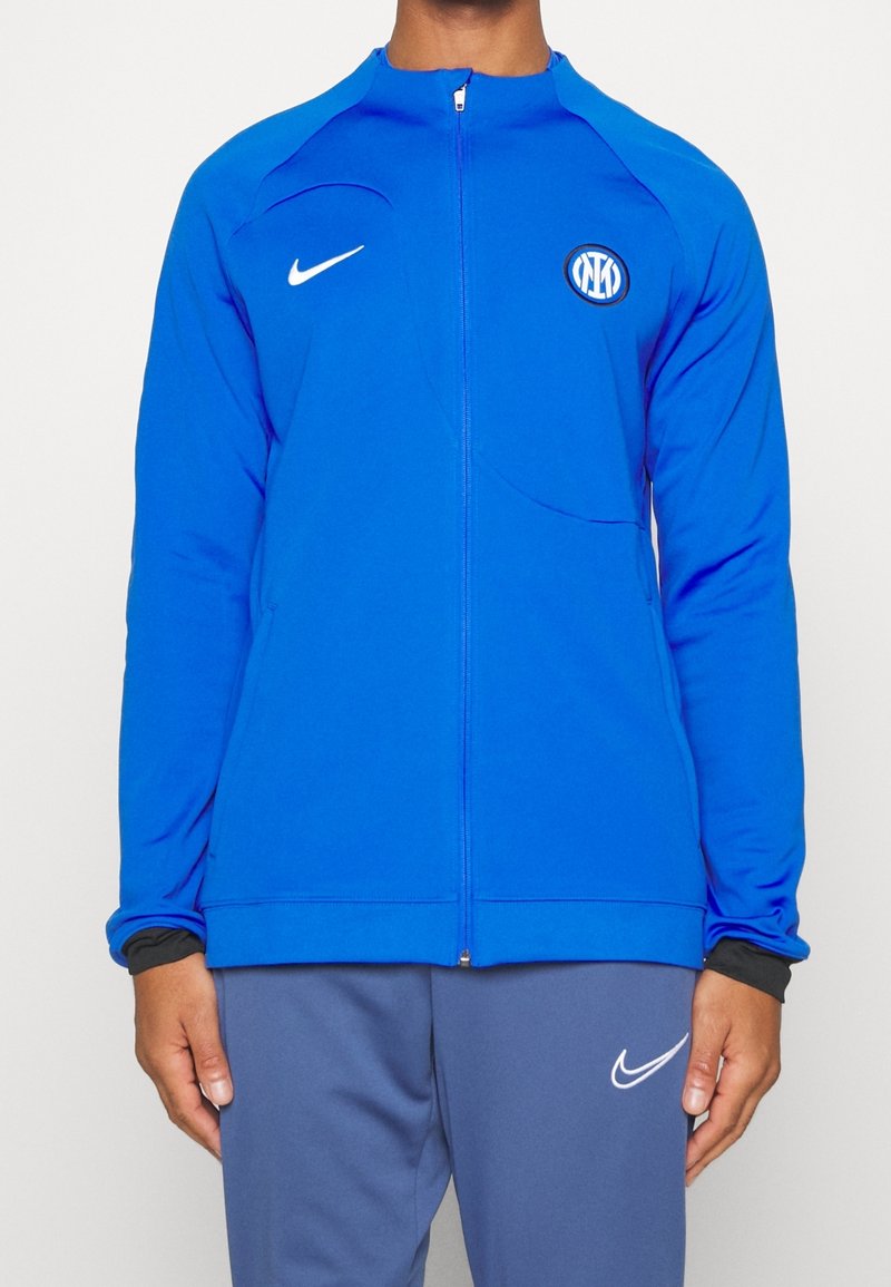 Homme portant une veste de sport bleue zippée avec le logo Nike et le blason du club de football Inter Milan, associée à un pantalon Nike bleu.