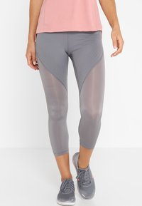 Graue Sportleggings mit Netzpaneelen und perforierten Details, in einem figurbetonten Design mit glatter Textur, kombiniert mit grauen Sportschuhen.