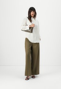 White button-up shirt, olive wide-leg pants, black heeled sandals. Brown textured handbag with diamond pattern. Model standing in a neutral background.