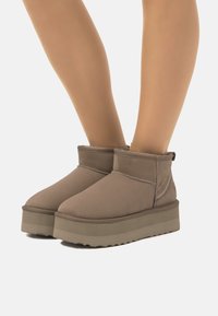 Botas marrones de altura hasta el tobillo con una superficie lisa y texturizada, que cuentan con una suela de plataforma y costuras en contraste a lo largo de las juntas.