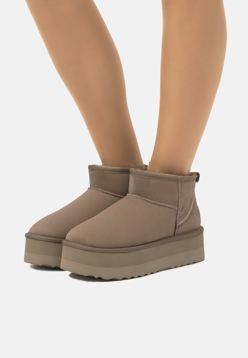 Botas marrones de altura hasta el tobillo con una superficie lisa y texturizada, que cuentan con una suela de plataforma y costuras en contraste a lo largo de las juntas.
