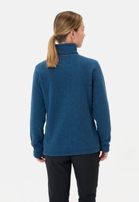 Giacca in pile blu, con colletto alto, maniche lunghe e vestibilità comoda. Evidente cucitura rossa sul retro.