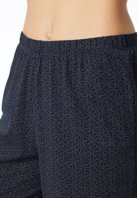 Marineblauwe broek met elastische tailleband, voorzien van een patroon in lichtere tinten. De stof lijkt zacht met een lichte glans en een gestructureerd detail.