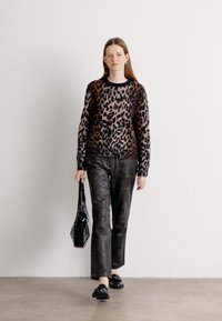 Pull en maille à imprimé léopard, pantalon noir et chaussures noires. Le modèle porte un sac à main noir. Texture lisse, manches longues, coupe décontractée.