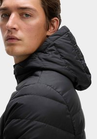 Sort puffertjakke med hætte, der har quiltet design og en glat, blank stoftekstur. Nærbillede af kraven og den øverste ryg.