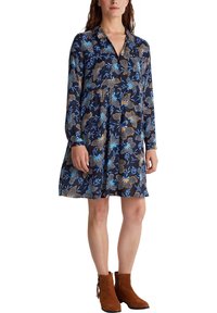 Abito navy a fantasia floreale con maniche lunghe, colletto con bottoni e silhouette svasata. Abbinato a stivaletti marroni per un contrasto.