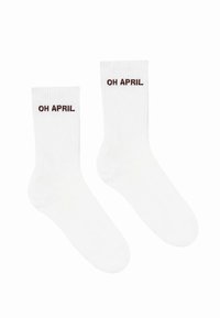 Hvide ribbede sokker med teksten "OH APRIL" i mørkebrunt. Designet har en klassisk form med højde til midten af læggen.