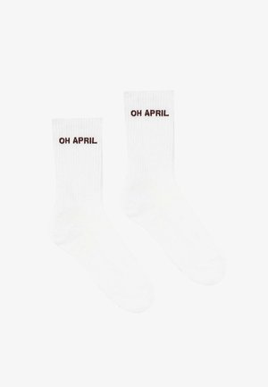 Baltas ribotās zeķes ar tumši brūnu tekstu "OH APRIL". Dizains ietver klasisku formu ar vidus teļu augstumu.