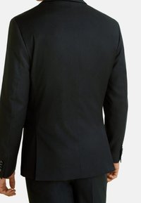 Veste de costume noire ajustée vue de dos. Dotée d'un tissu texturé, d'une coupe slim et d'une fente unique en bas. Boutons décoratifs aux poignets.