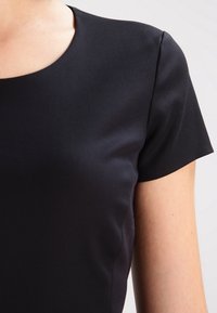 Haut noir à manches courtes avec un col rond. Fabriqué en tissu lisse avec une coupe ajustée, mettant en avant un style minimaliste.