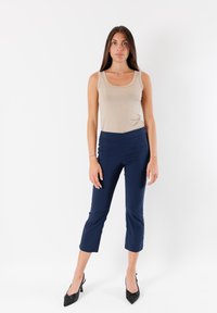 Top aderente beige abbinato a pantaloni blu navy alla caviglia, con una texture liscia e un taglio dritto, completato da tacchi neri.