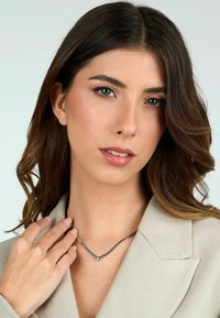 Collana d'argento con un design a forma di V che presenta un piccolo accento quadrato, indossata da una persona con capelli castano chiaro e trucco naturale.