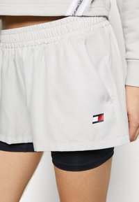 Shorts deportivos gris claro con cintura elástica, bolsillos laterales y un pequeño logo con detalles en rojo, blanco y azul.