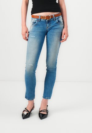 Skinny blue jeans with fading and distressed details, paired with black patent leather pointed-toe shoes and a brown belt.