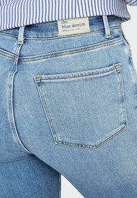 Heledad sinine teksapüksid klassikalise viie taskuga disainiga, milles on tagatasku peene õmblusega ja silt, millel on kiri "the blue denim".