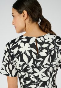 Vestido negro con patrones florales blancos, de mangas cortas y un detalle en forma de llave en la parte de atrás, hecho de una tela ligera y suave.
