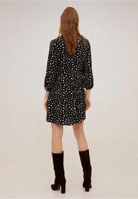 Robe noire à taches blanches irrégulières, manches longues et taille cintrée. Associée à des bottes noires montantes jusqu'aux genoux. Fond uni.