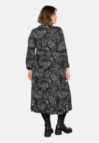 Vestito lungo nero e bianco con motivo, maniche lunghe, forma fluente e vita aderente, abbinato a stivali alla caviglia chunky neri.