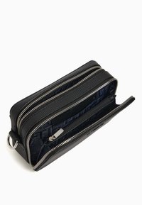 Portefeuille en cuir noir avec plusieurs compartiments zippés, extérieur texturé et doublure en tissu à motifs présentant un design géométrique bleu.