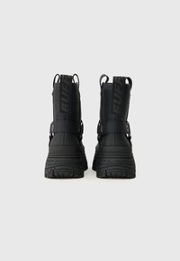 Czarne, masywne buty na platformie z logo "BUFFALO" na pętlach i podeszwach, widok od tyłu na jednolitym białym tle.