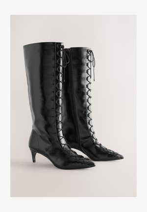 Zwarte leren kniehoge laarzen met spitse neus, voorzien van een veterdetail langs de zijkant en een kleine kittenhak.