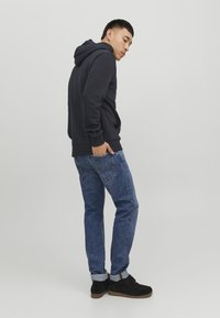 Felpa blu marina con tasca a marsupio e polsini a costine, abbinata a jeans blu sbiaditi e scarpe in pelle scamosciata nera con suola spessa.