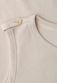 Top beige côtelé sans manches avec un col rond et une bretelle d'épaule fixée par un bouton doré texturé.