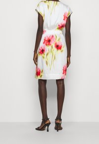 Kort vit klänning med blommönster i rosa och grönt, åtsittande midja och korta ärmar; ihop med svarta högklackade sandaler.