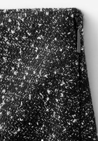 Material tricotat alb-negru texturat, cu un model pătat, având o finisare elegantă cu fermoar. Materialul pare moale și călduros.