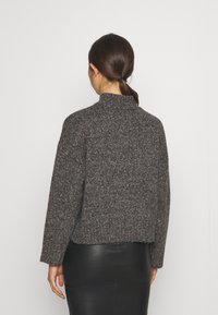 Grauer strukturierter Pullover mit hohem Kragen und lockerem Schnitt. Mit einem Strickmuster, kontrastierenden Farbklecksen und kurzer Länge.