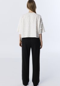 Top corto bianco strutturato con rouches orizzontali, abbinato a pantaloni neri a gamba larga con strisce laterali e tasche.