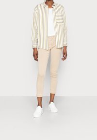 Camisa de botones a rayas en verde oliva y blanco, combinada con pantalones cortos beige y zapatillas blancas. Tela suave, corte relajado, bolsillo frontal.