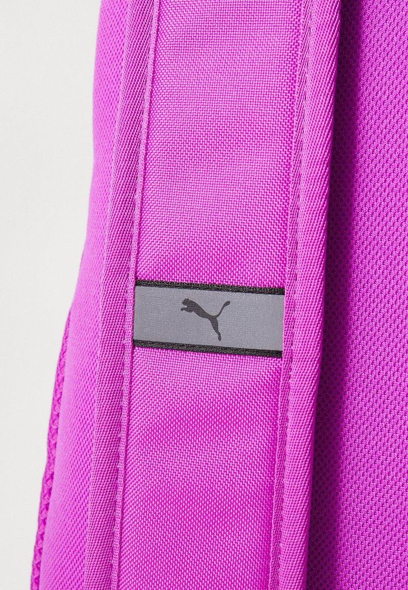 Sac en tissu rose avec une surface texturée, arborant un logo Puma noir sur une étiquette rectangulaire grise. Comprend des bords cousus pour une durabilité accrue.