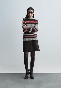 Multifarvet stribet sweater i grå, rød og brun; parret med en mørkebrun ruskindnederdel med to forlommer. Sorte ankelstøvler.