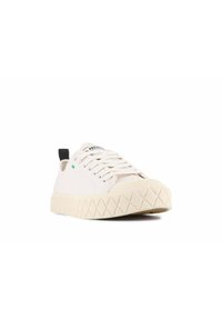 Bílé tenisky na šněrování s texturovanou krémovou gumovou podrážkou, plochým designem, černým patním poutkem a zeleným akcentem na boku.